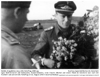 Egon Stoll-Berberich mit Kameraden, Blumensträußen, einer Flasche Alkohol und einem Pokal als Geschenk kurz nach der Rückkehr von seinem 500. Feindflug am 31. August 1943 in Seschtschinskaya. NLESB_Kriegsbilder_lose_500_Feindflug_0004.