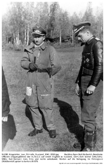 Offiziere (Flugzeugführer) der III./St.G.1 auf einem Flugfeld in Russland, vermutlich Winter 1941/1942. Mitte: Karl-Hermann Lion, links und rechts unbekannt. Warten auf die Verlegung, im Hintergrund (Waldbereich) getarnte Junkers JU 87B. NLESB_Kriegsbilder_lose_Filmrolle_Russland_1941_0010