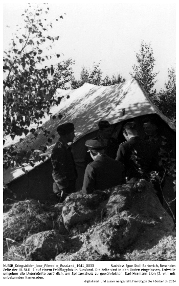 Zelte der III./St.G. 1 auf einem Feldflugplatz in Russland. Die Zelte sind in den Boden eingelassen, Erdwälle umgeben die Unterkünfte zusätzlich, um Splitterschutz zu gewährleisten. Karl-Hermann Lion (3. v. l.) mit unbekannten Kameraden. NLESB_Kriegsbilder_lose_Filmrolle_Russland_1941_0033