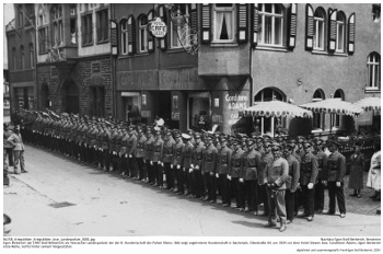 Egon Berberich (ab 1943 Stoll-Berberich) als Hessischer Landespolizist bei der 8. Hundertschaft der Polizei Mainz. Bild zeigt angetretene Hunderschaft in Bacherach, Oberstraße 64, um 1934 vor dem Hotel Giesers bzw. Conditorei Adams; Egon Berberich erste Reihe, rechts hinter seinem Vorgesetzten. NLESB_Kriegsbilder_Kriegsbilder_lose_Landespolizei_0001